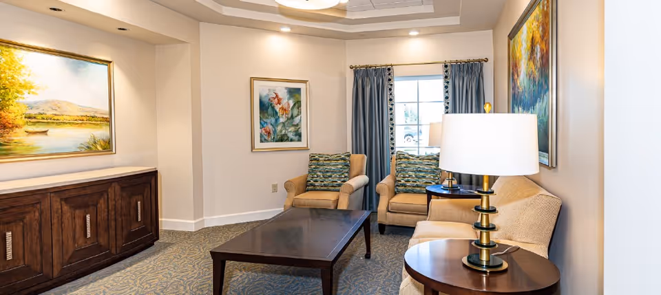 Bright seating area with upholstered chairs and sofa around a coffee table, side lamp and framed artwork on the walls.