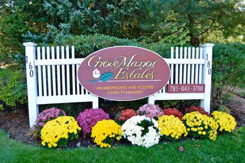 Grove Manor Estates sign with white picket fence and colorful flowers in front