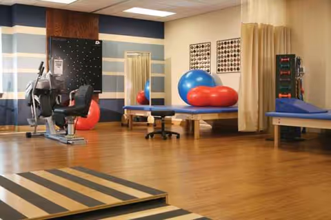 Rehabilitation gym with exercise equipment, therapy balls, balance boards, and mats