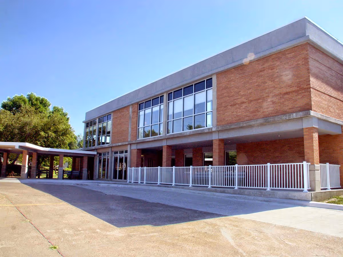 Front exterior of a two-story brick building with large windows, a covered drop-off canopy and white railing.