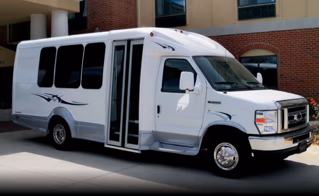 White passenger shuttle van parked in front of a brick-faced building entrance.