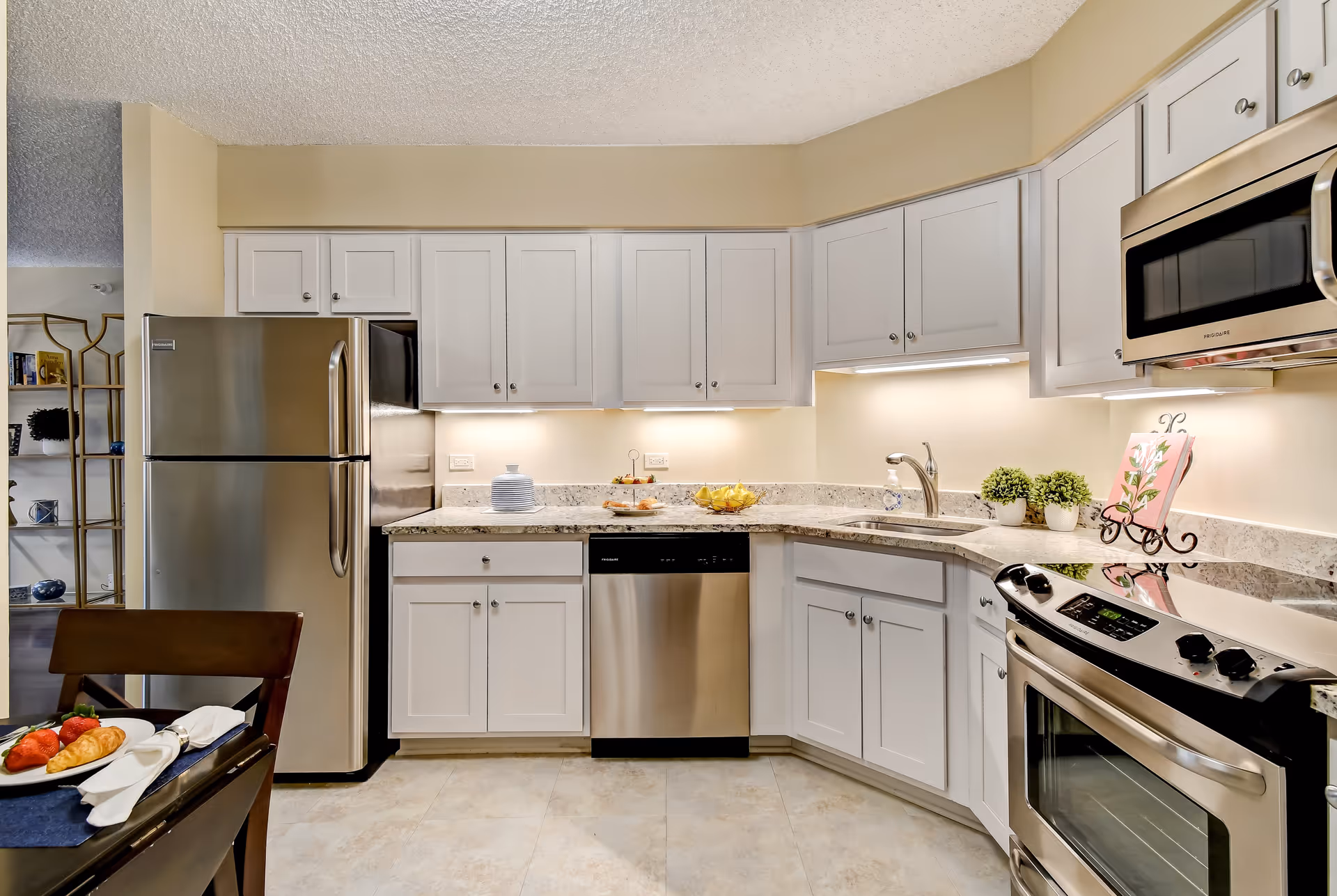 Modern kitchen with stainless steel appliances, white cabinets, and granite countertops with a small dining table visible.
