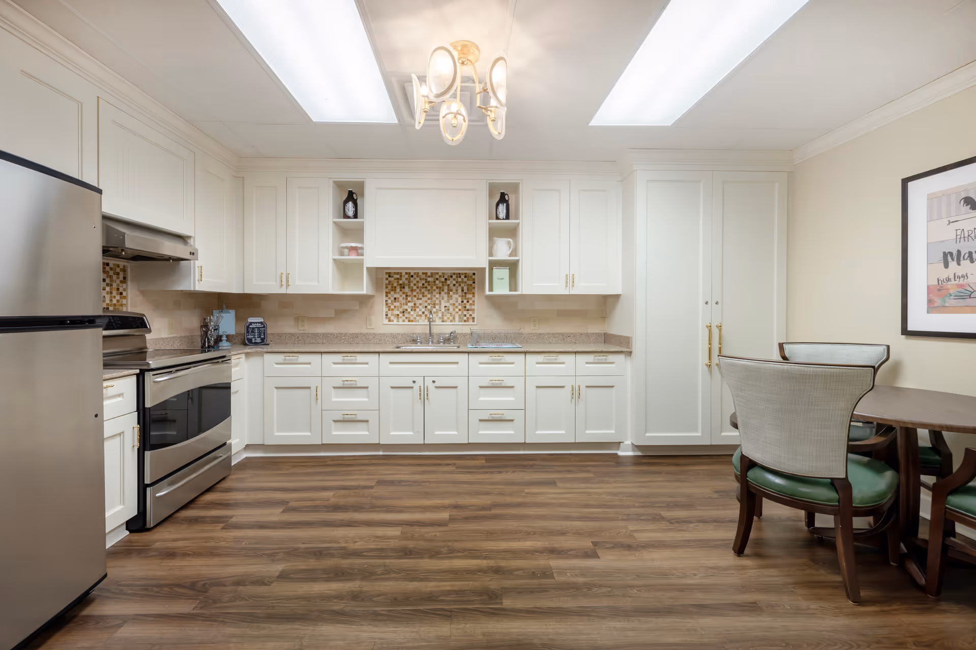 Bright kitchen with white cabinetry, stainless steel appliances, wood floors, and a small dining table with chairs.