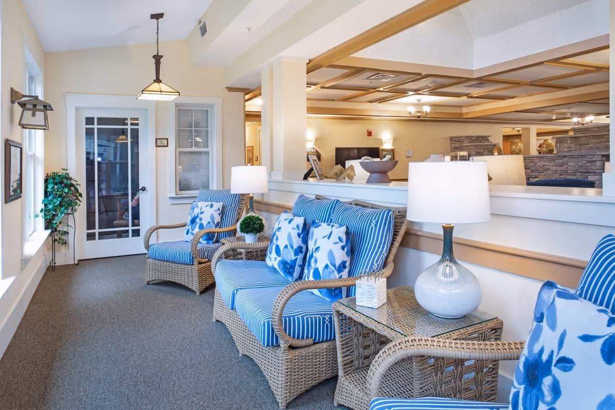 Bright seating area with wicker chairs in blue-striped cushions, side tables with lamps, and a view into a communal lobby.