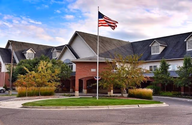 Front exterior view of Addington Place of Clarkston building with a circular driveway, landscaped greenery, and an American flag on a flagpole in the center.