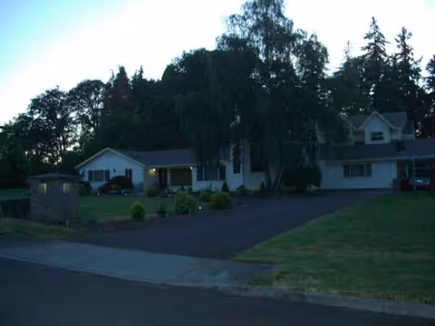 Exterior view of a single-story senior living facility with a driveway, lawn, and trees.
