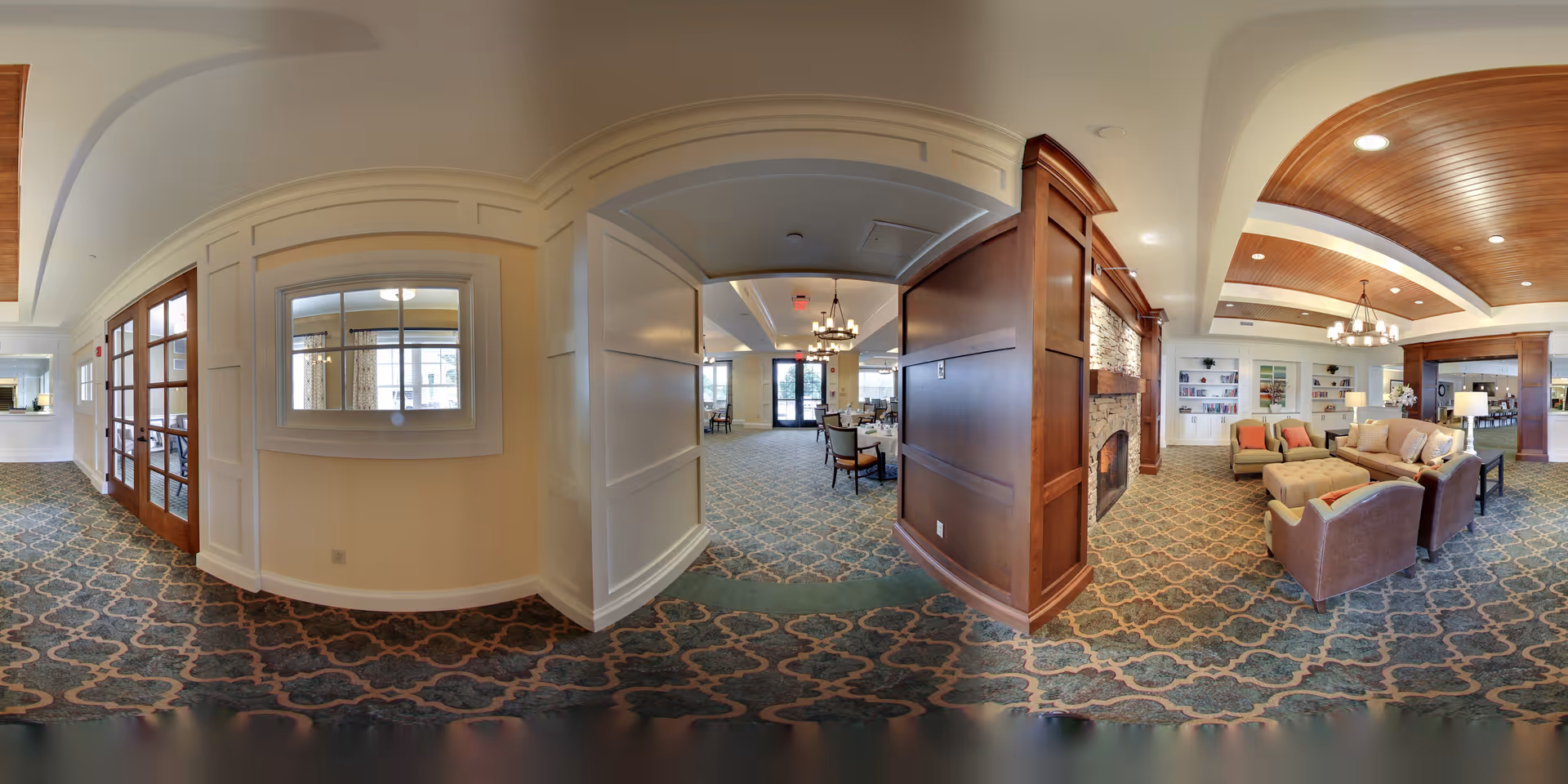 Spacious communal lounge and dining area with upholstered seating, a fireplace, and wood-paneled ceilings.