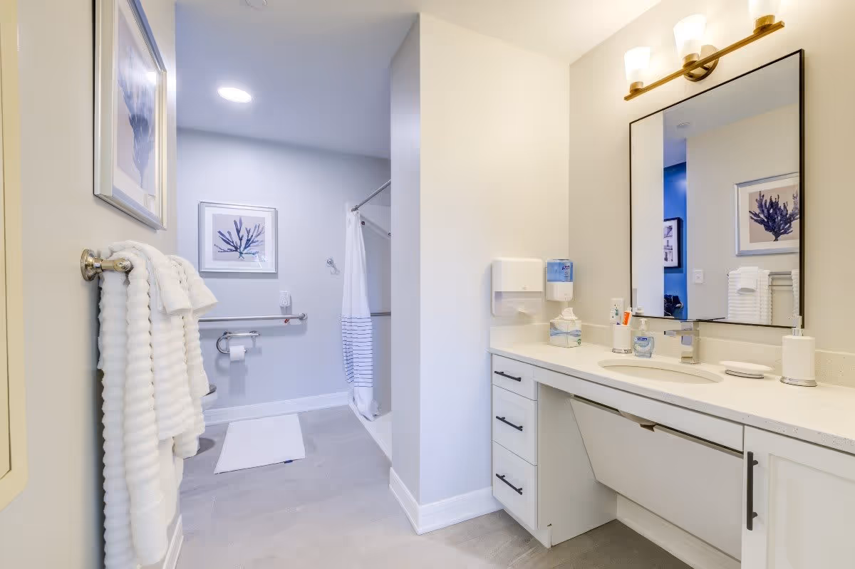 A modern bathroom featuring a white vanity with a mirror, neatly arranged towels, and decorative wall art. The space includes a shower area with a curtain and a clean, minimalist design.