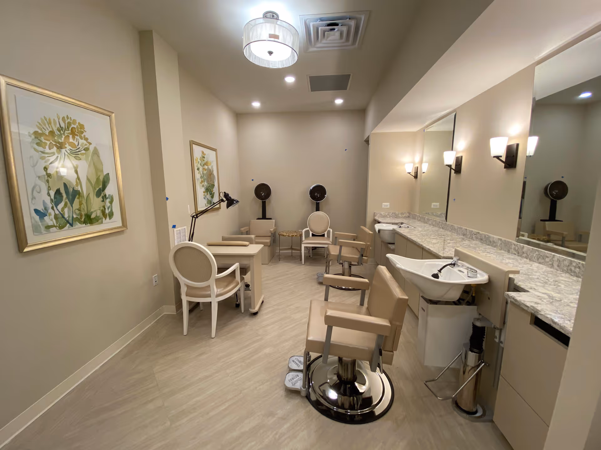 Salon-style grooming room with styling chairs, wash sinks, mirrors, a manicure table and framed botanical art.