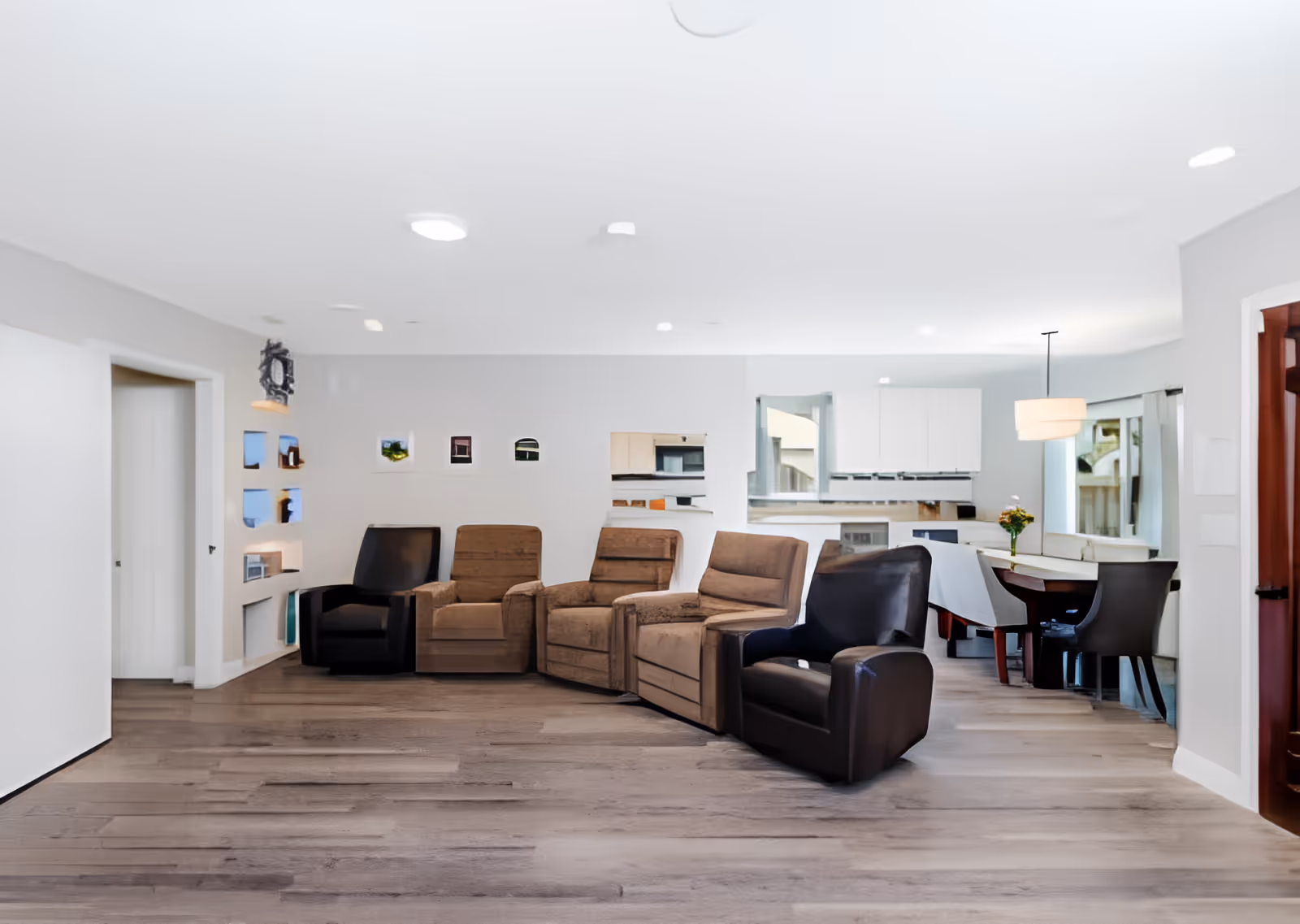 Bright open communal living area with a row of recliner chairs facing a dining area and kitchen in the background.