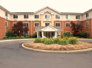Brick senior living building with central entrance and circular landscaped driveway with flowers.
