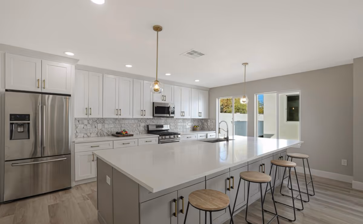 Bright modern kitchen with a large white island, pendant lights, stainless steel appliances and several bar stools.