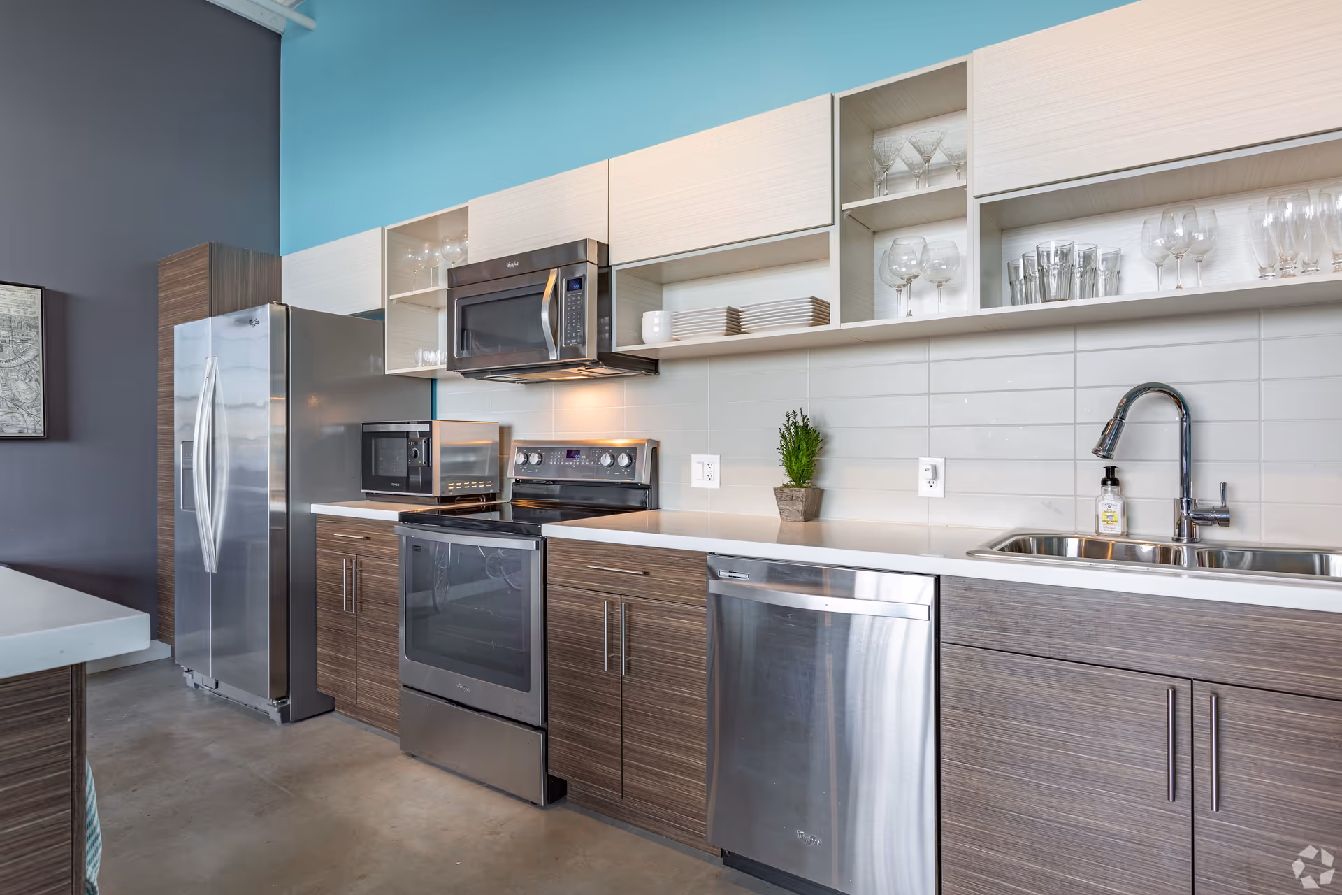 Modern stainless-steel kitchen with refrigerator, oven, microwave, dishwasher, sink and open shelving.