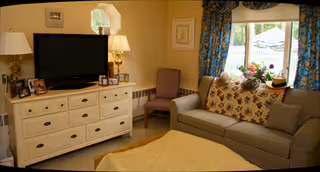 Cozy living room featuring a sofa, TV stand, lamps, and a blue-curtained window.