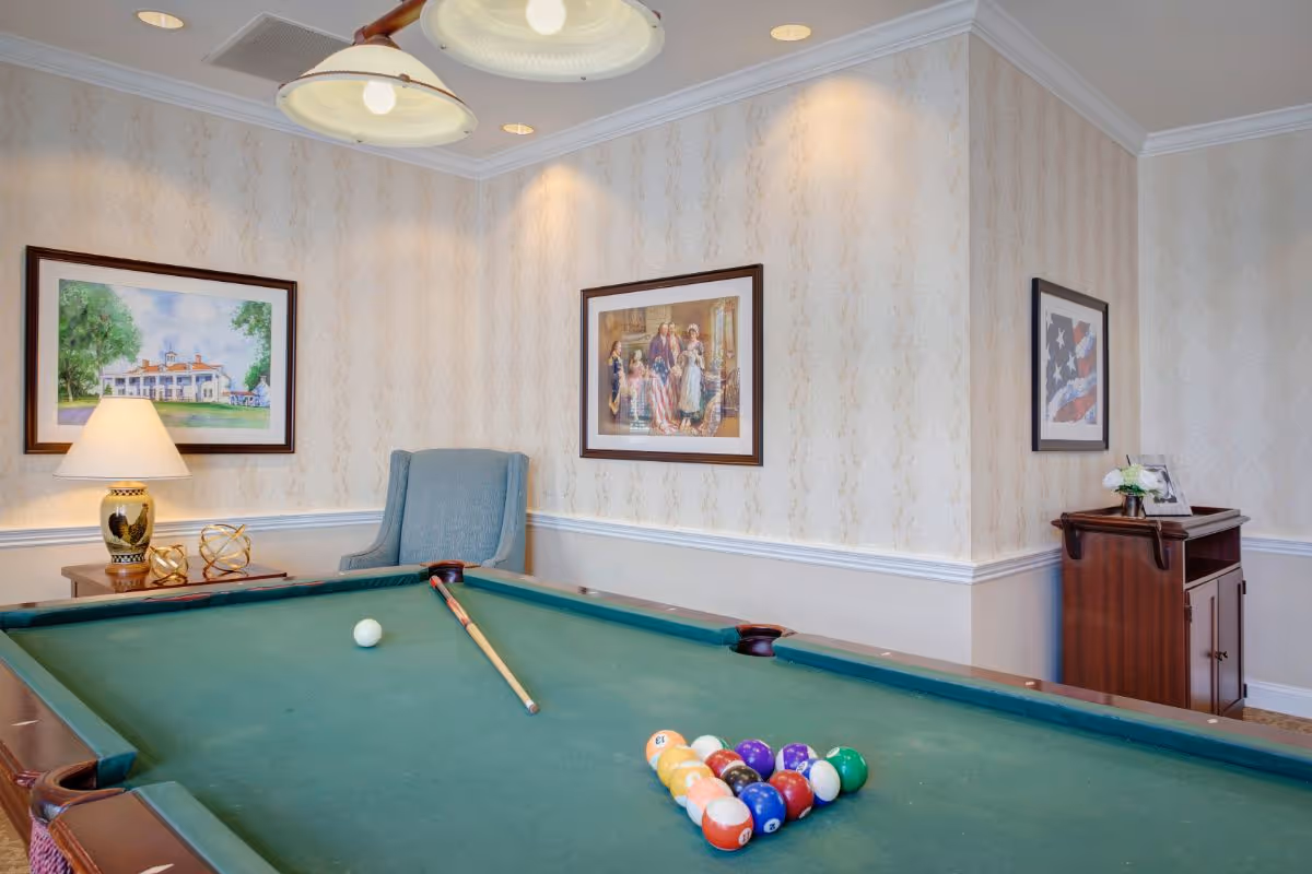 Interior recreation room with a pool table, cue stick, framed artwork, and seating against wallpapered walls.
