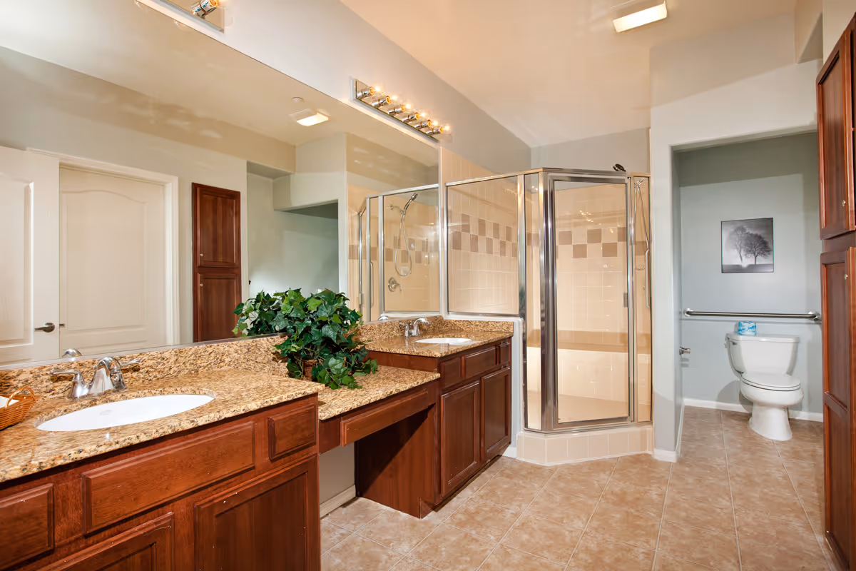 Spacious bathroom with a granite double-sink vanity and wood cabinets, glass corner shower, and toilet.