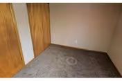Empty room with beige walls, brown carpet flooring, and two wooden closet doors on one side.