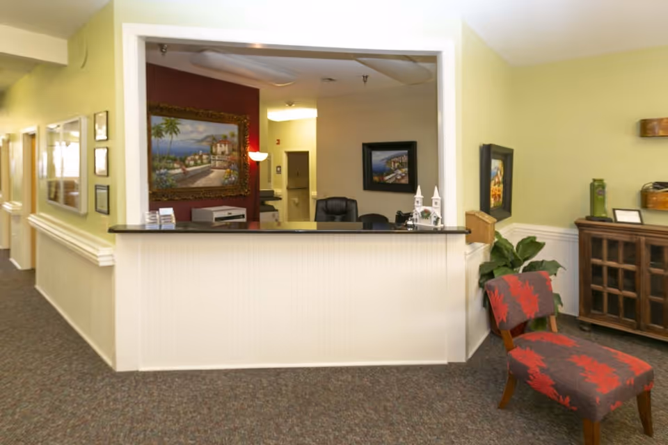 Interior reception area with a front desk, patterned chair, framed artwork, and a hallway.