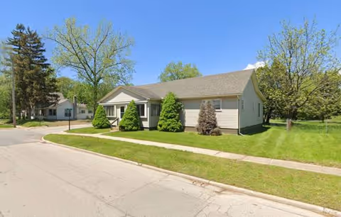 A single-story beige senior living facility with a manicured lawn and trees.