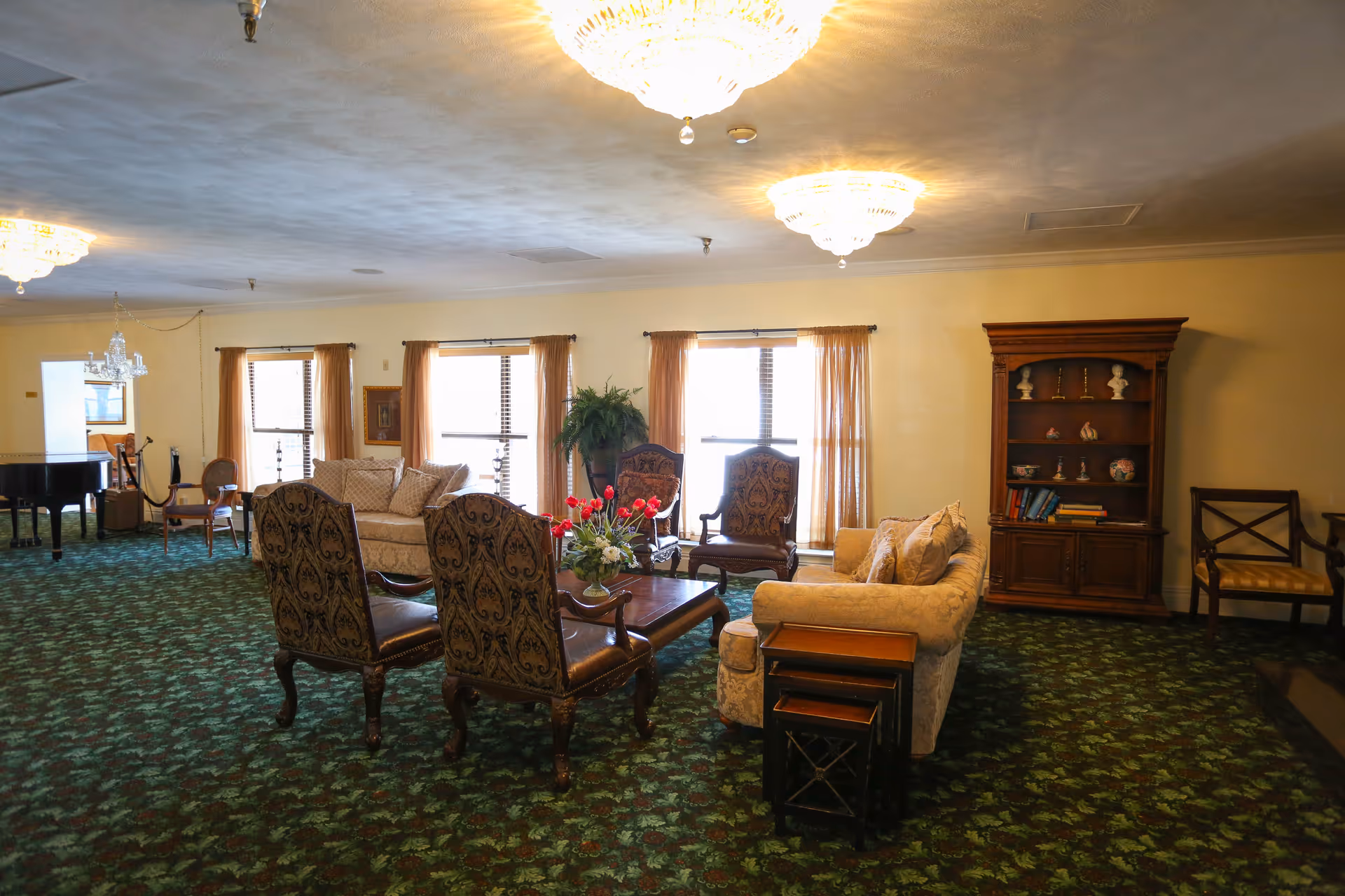 Spacious, formally furnished common living room with sofas, upholstered chairs, a coffee table, bookcase and chandeliers.