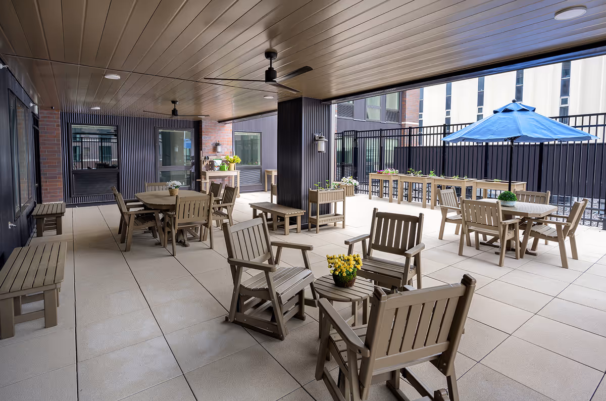 Covered outdoor courtyard with multiple tables, chairs, planters and a blue umbrella.