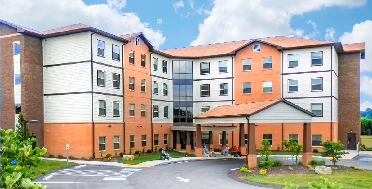 Front exterior of a four-story brick and siding senior living building with a covered entrance and driveway.