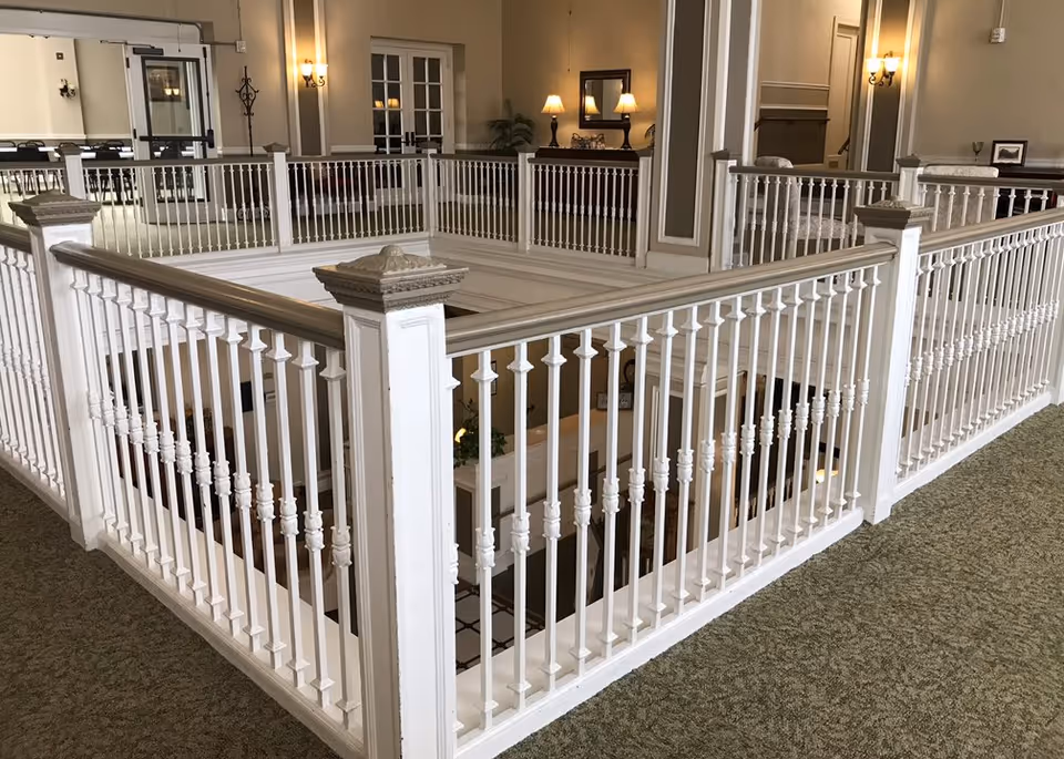 White decorative railing encloses a stairwell in a spacious, well-lit indoor lobby.