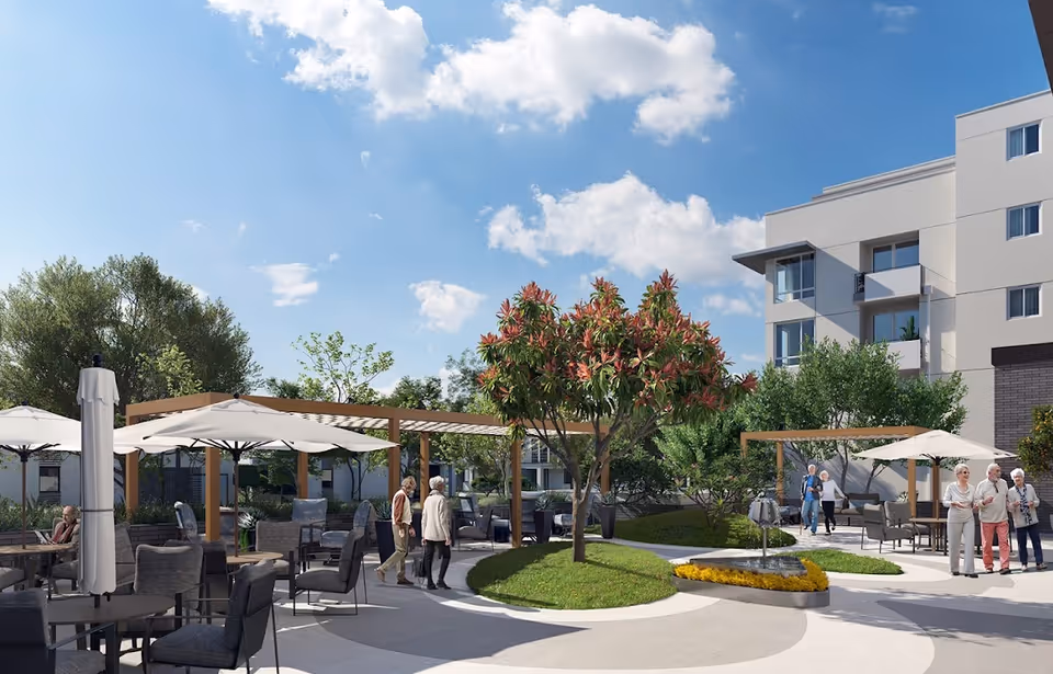 Outdoor courtyard with patio seating, umbrellas, pergolas, a central tree, and several people walking and sitting.