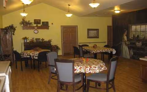 A cozy dining room with round tables, floral tablecloths, and chairs in a senior living facility.