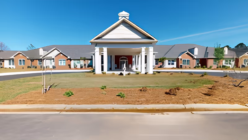 Front exterior of a single-story senior living facility with a columned portico, circular driveway, and landscaped lawn.