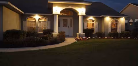 Exterior view of a single-story senior care home at dusk with lit entrance and landscaping.