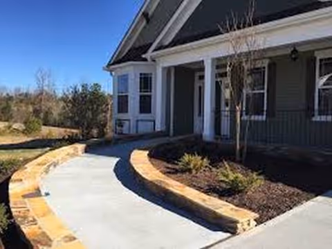 Curved concrete walkway leads to the front entrance of a gray and white senior living building.