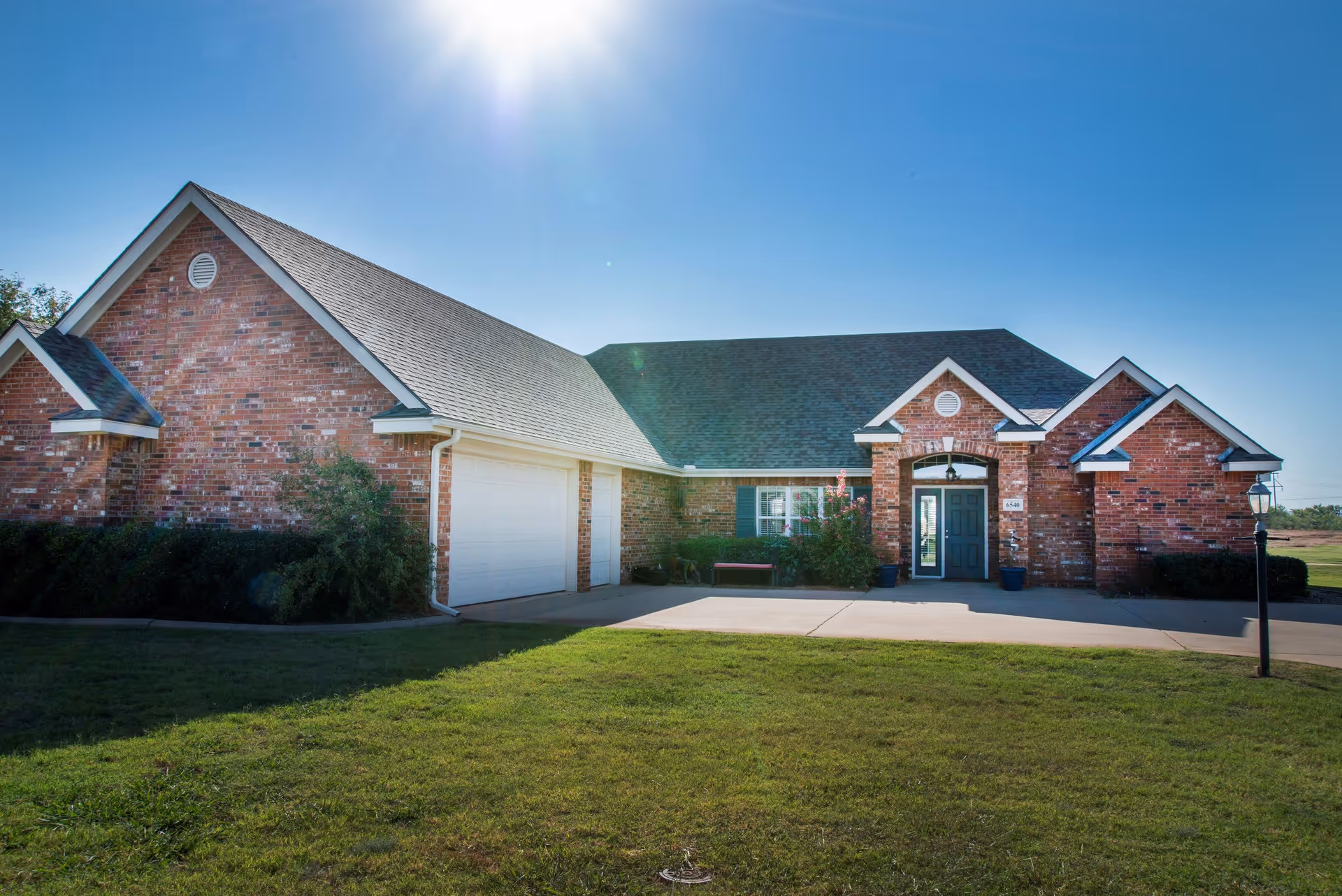 Front view of a single-story brick building with an attached garage, driveway, and lawn under a sunny blue sky.