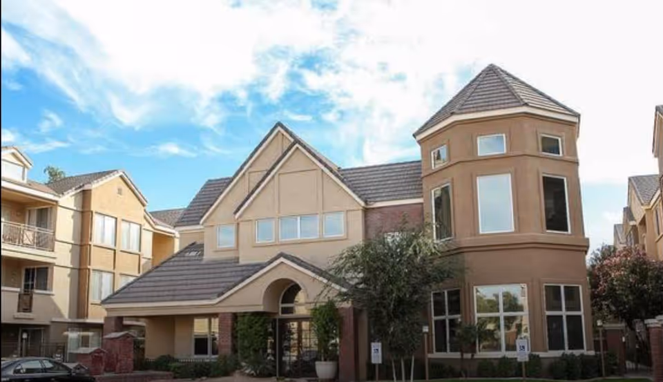 Front exterior of a multi-story senior living building with a turret-like corner and main entrance under a pitched roof.