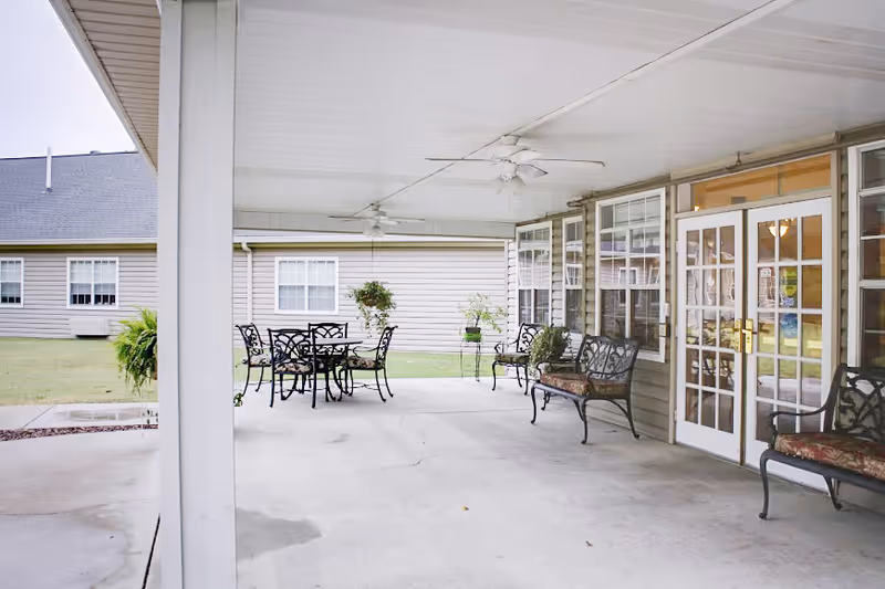 Covered outdoor patio with metal tables and benches, ceiling fans, and French doors leading into the building.