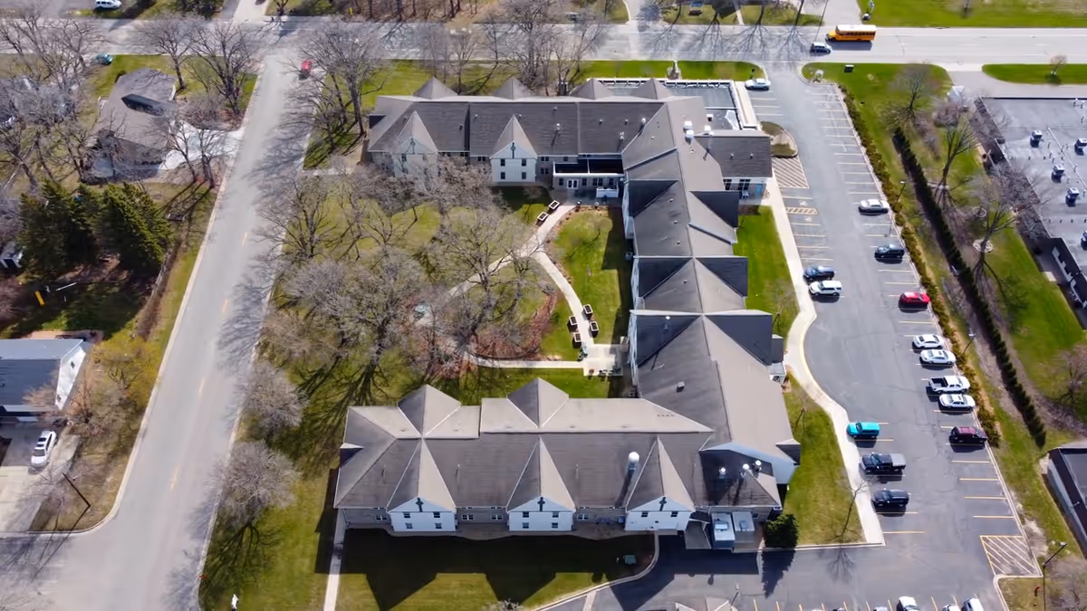 Aerial view of Nelson Gables by Vivie facility showing a large building with multiple roof sections, surrounded by trees, a parking lot with several cars, and adjacent roads.