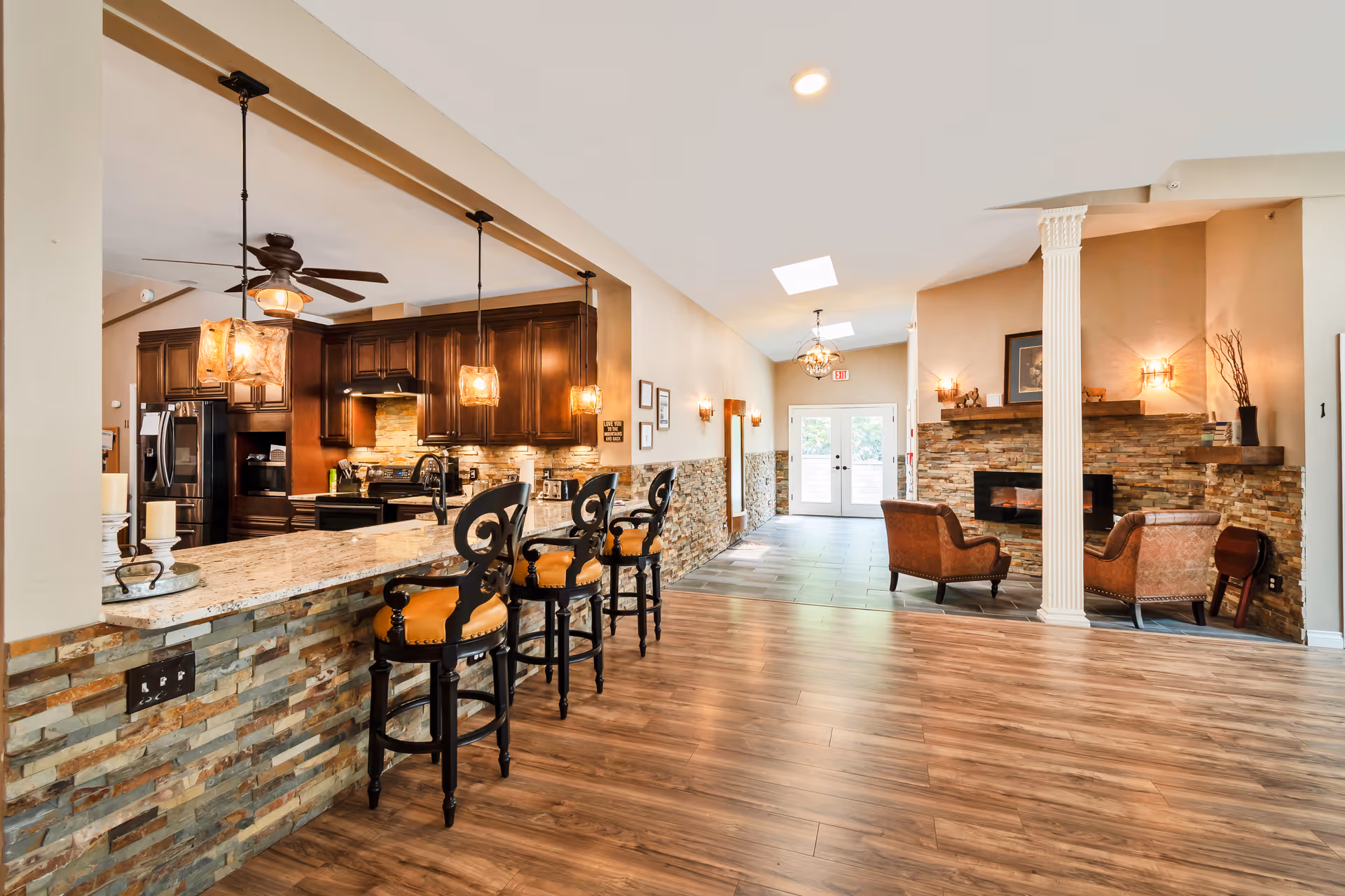 Open communal interior space with a breakfast bar and stools, dark wood kitchen cabinets, and a cozy seating area with a fireplace.