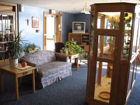 Cozy senior living lounge with sofa, plants, and display cabinet.