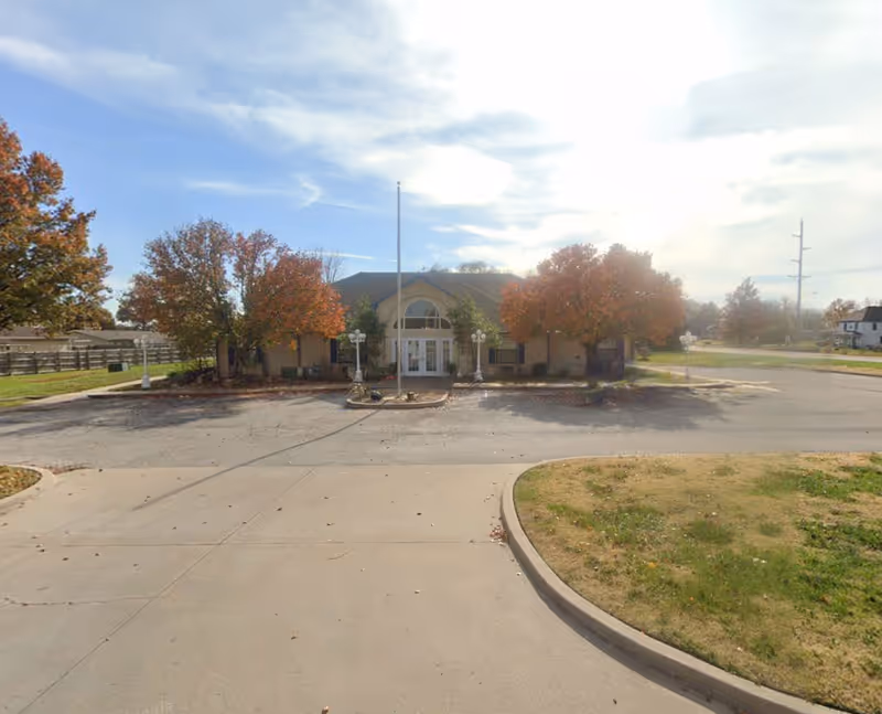 Front exterior view of a single-story senior living facility with a circular driveway and trees.