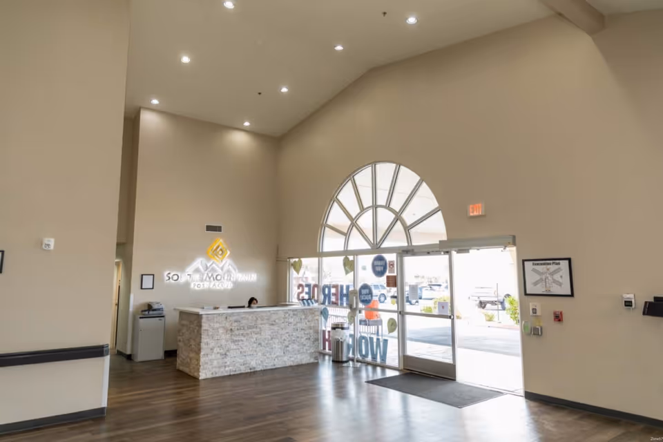 Spacious reception lobby with a stone-faced front desk, tall arched entrance windows, and an illuminated facility logo on the wall.