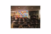 Communal dining room with rows of wooden tables and chairs facing colorful stained-glass style panels and a piano.