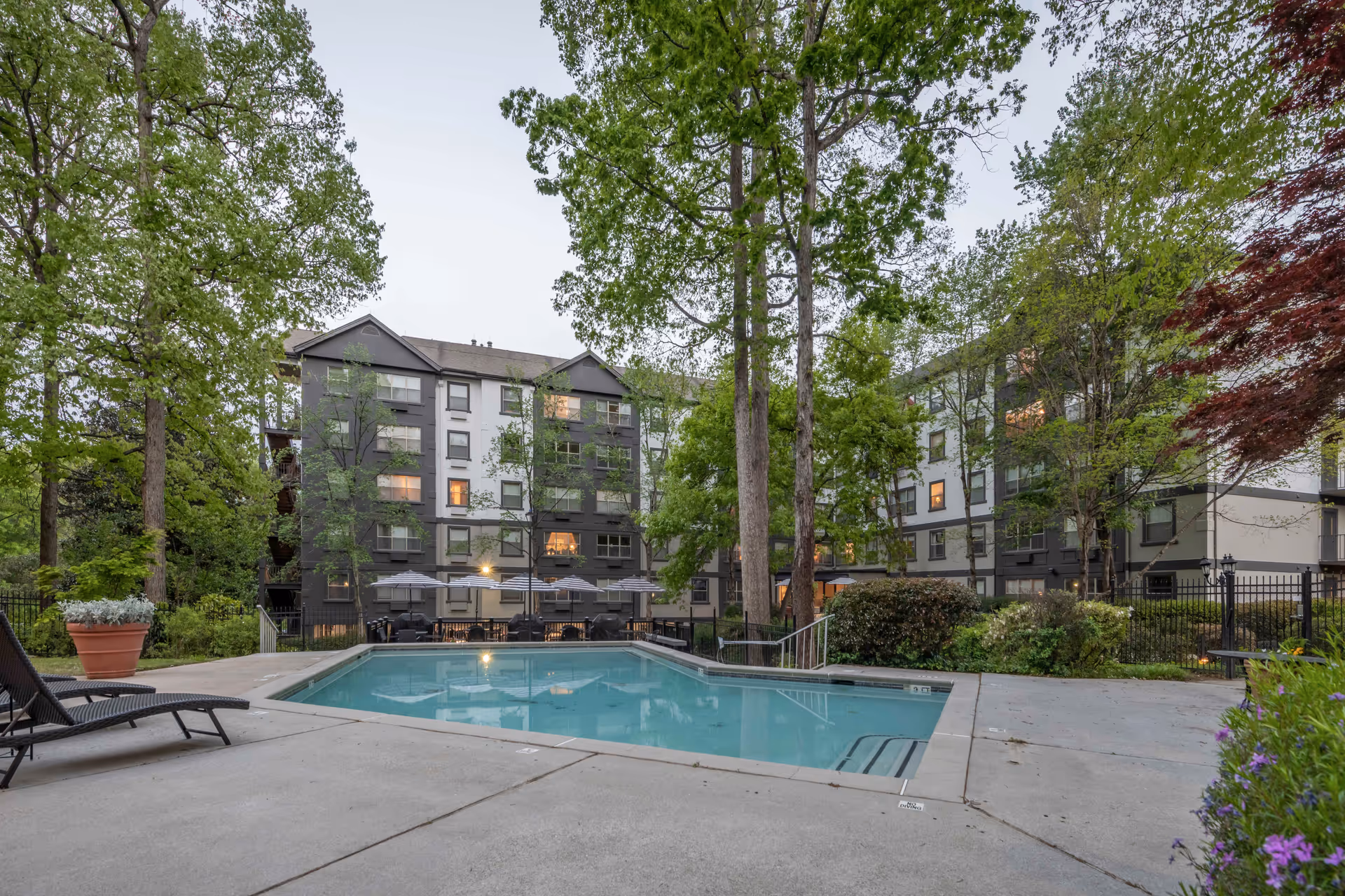 Outdoor courtyard with a swimming pool in front of a multi-story apartment building surrounded by trees.