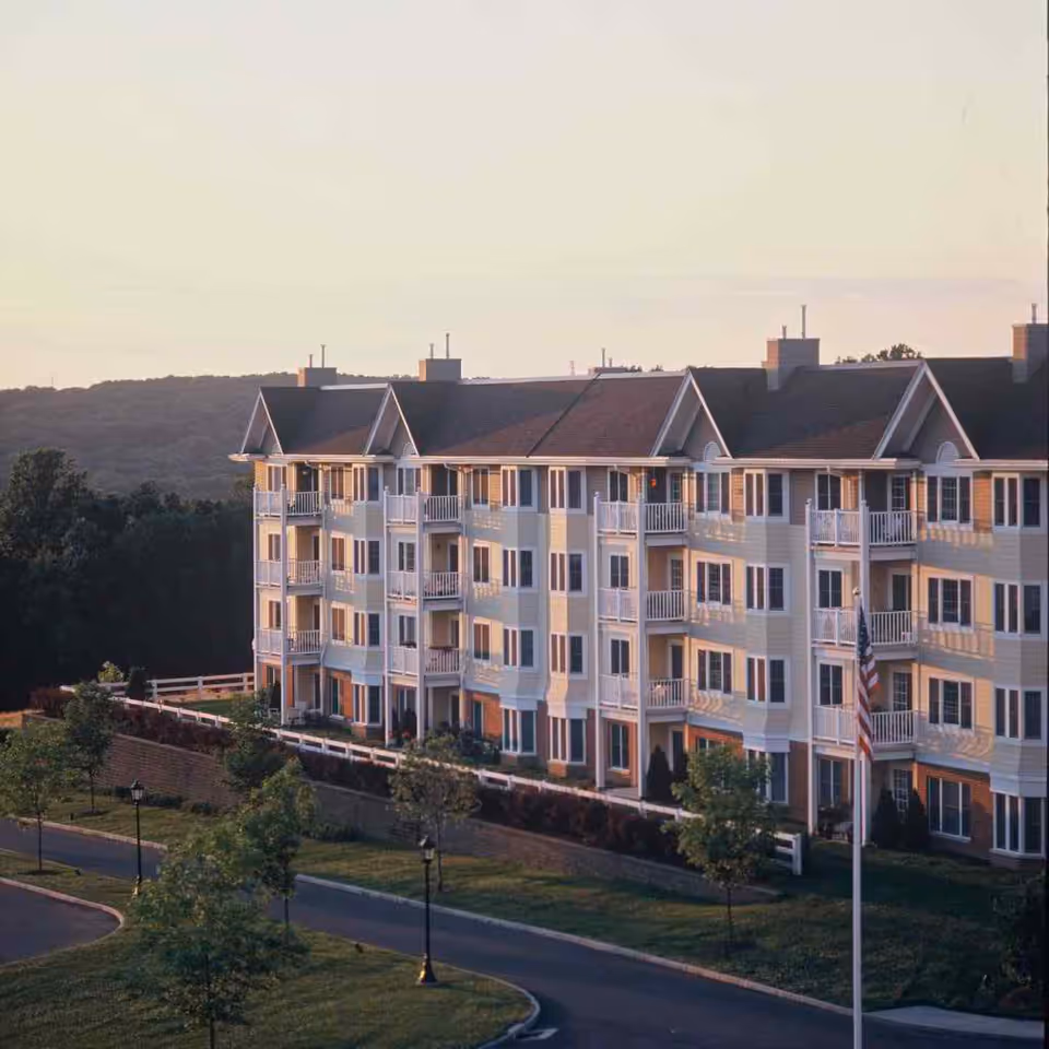 A multi-story Meadow Ridge senior living building exterior with balconies, landscaped grounds, and an American flag.