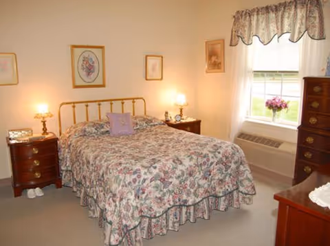Bedroom with a floral bedspread on a double bed, brass headboard, matching nightstands with lamps, and a window with a valance.