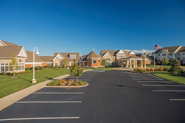 Exterior view of a senior living campus with brick buildings, parking lot, and blue sky.