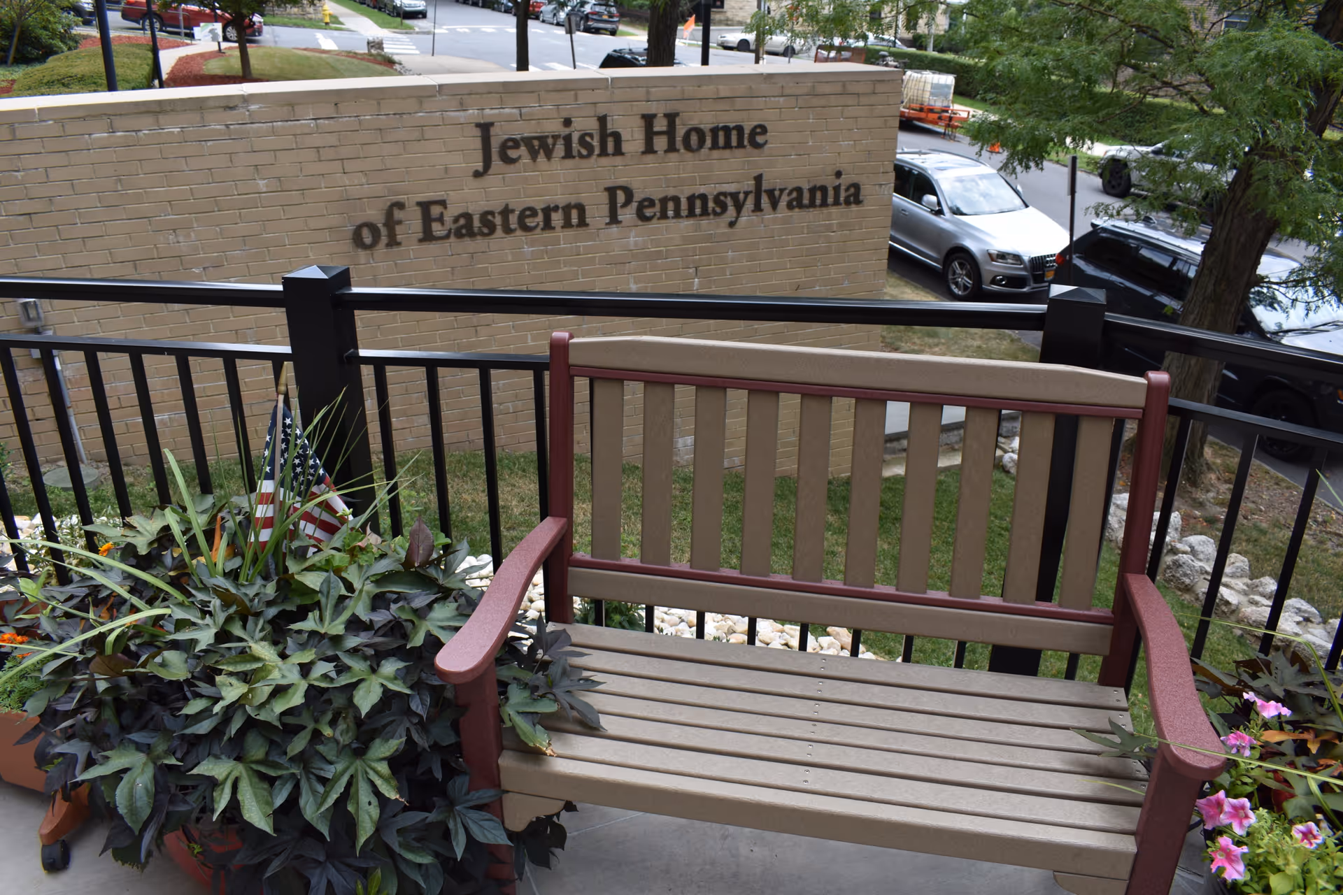 A bench and potted plants on a patio in front of a brick sign reading "Jewish Home of Eastern Pennsylvania".