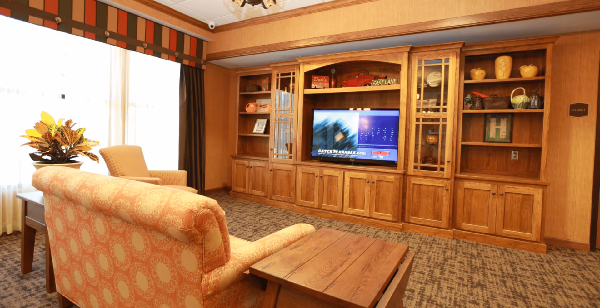 Cozy common living room with upholstered seating facing a large wooden built-in entertainment center and TV.