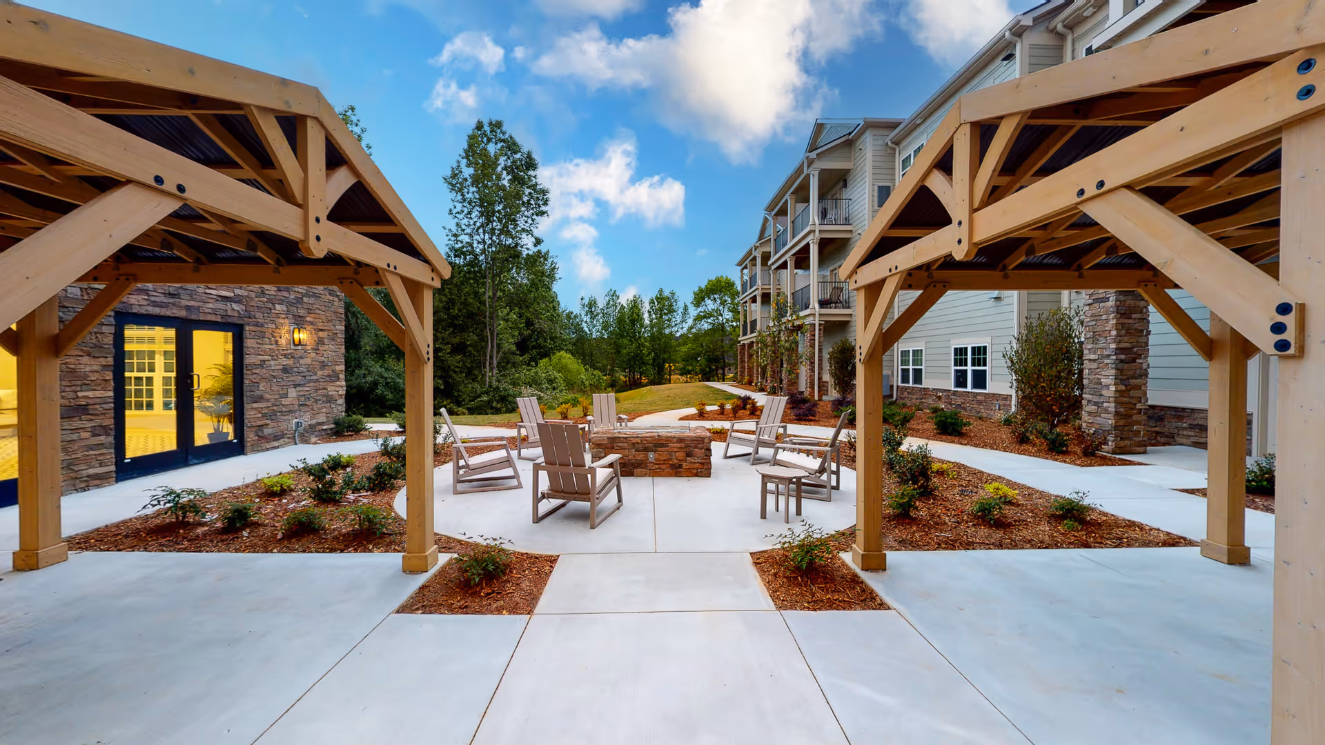 Outdoor courtyard with wooden pergolas, Adirondack chairs arranged around a central fire pit and the apartment building with balconies in the background.
