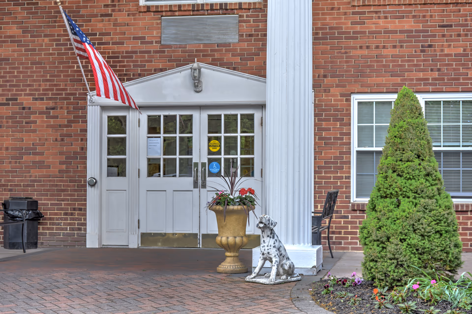 Exterior entrance of The Court of Saint James with flag, columns, and potted plant.
