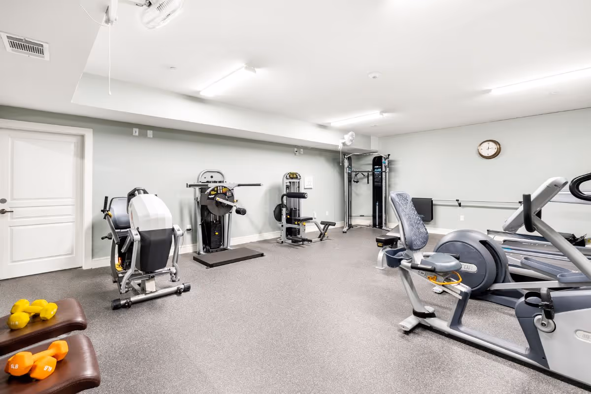 Well-lit interior fitness room with exercise machines, recumbent bikes, treadmills, and free weights.